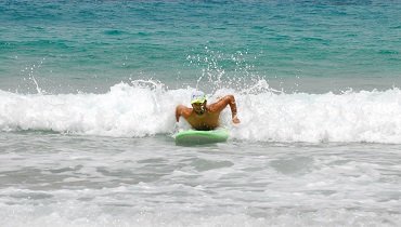 Erst wenn du spürst, dass dich die Welle mitnimmt und du an Geschwindigkeit gewinnst, hörst du auf mit paddeln und stützst dich mit den Händen nahe der Rails deines Surfbretts nach oben.